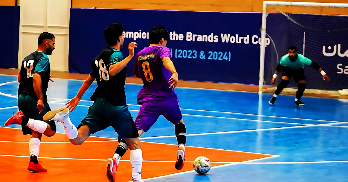 An Afghanistan futsal player in purple advances with the ball during a game in an indoor arena