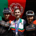 Fariba Hashimi wearing her Asian Games silver medal between two Afghan cyclists in front of the Afghan flag