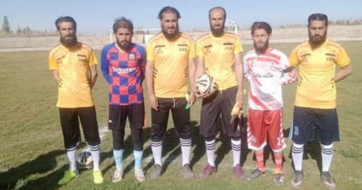 Six players and match officials on a football field in Paktika.